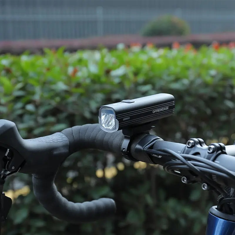 Bicycle handlebar with a light attached, blurred greenery in the background