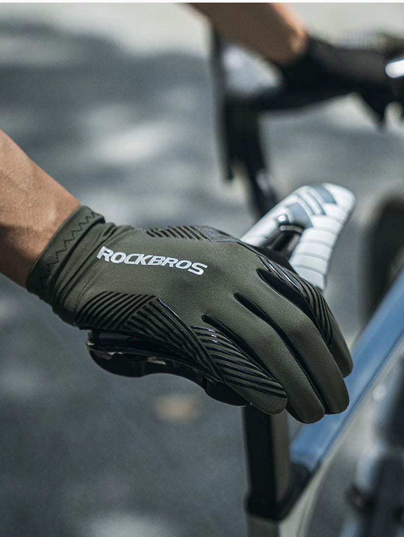 Black cycling glove with 'RockBros' branding held by a cyclist on a blurred road background